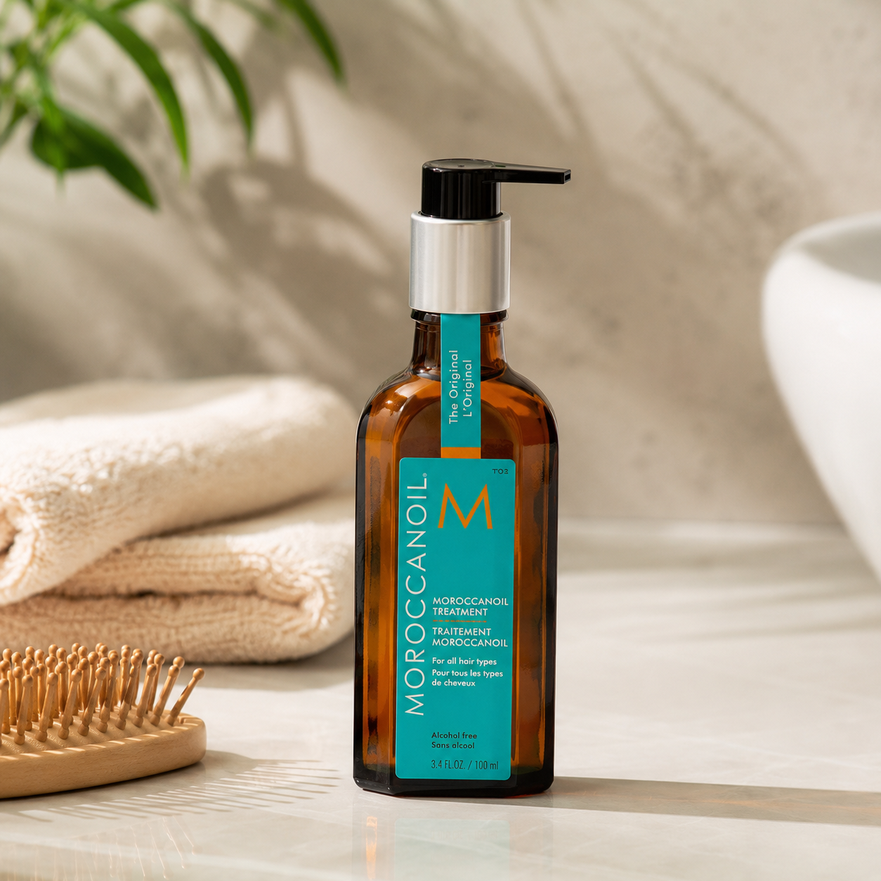 Moroccanoil Treatment oil bottle on a light cream bathroom-style surface with towel, hairbrush and soft natural lighting for a hair care blog.