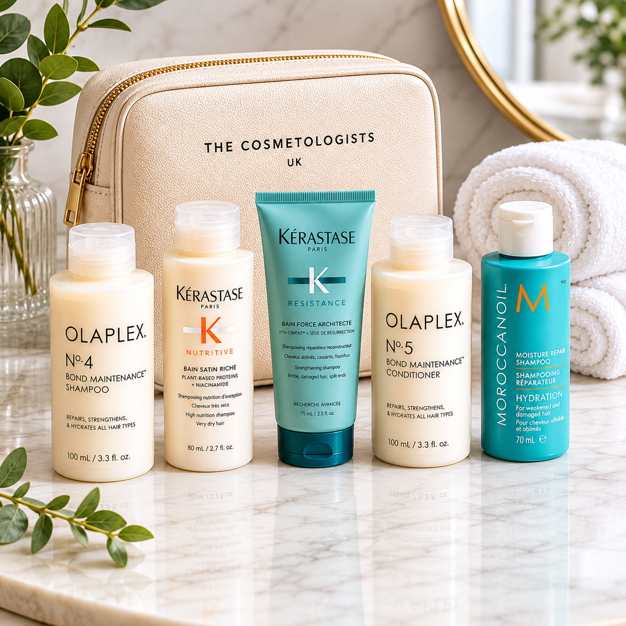 Luxury travel-size shampoos and mini haircare essentials including Olaplex, Kérastase and Moroccanoil products displayed beside a premium cosmetic travel bag on a glossy marble surface with fresh botanical accents in a bright spa-inspired setting.