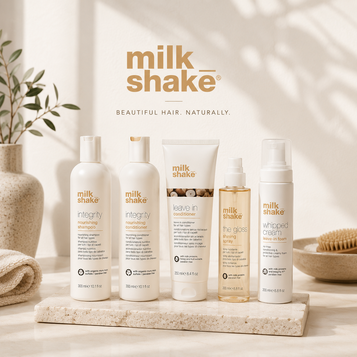 Luxury milk_shake haircare products including shampoo, conditioner, leave-in treatment and gloss spray displayed on a soft beige spa-inspired background.