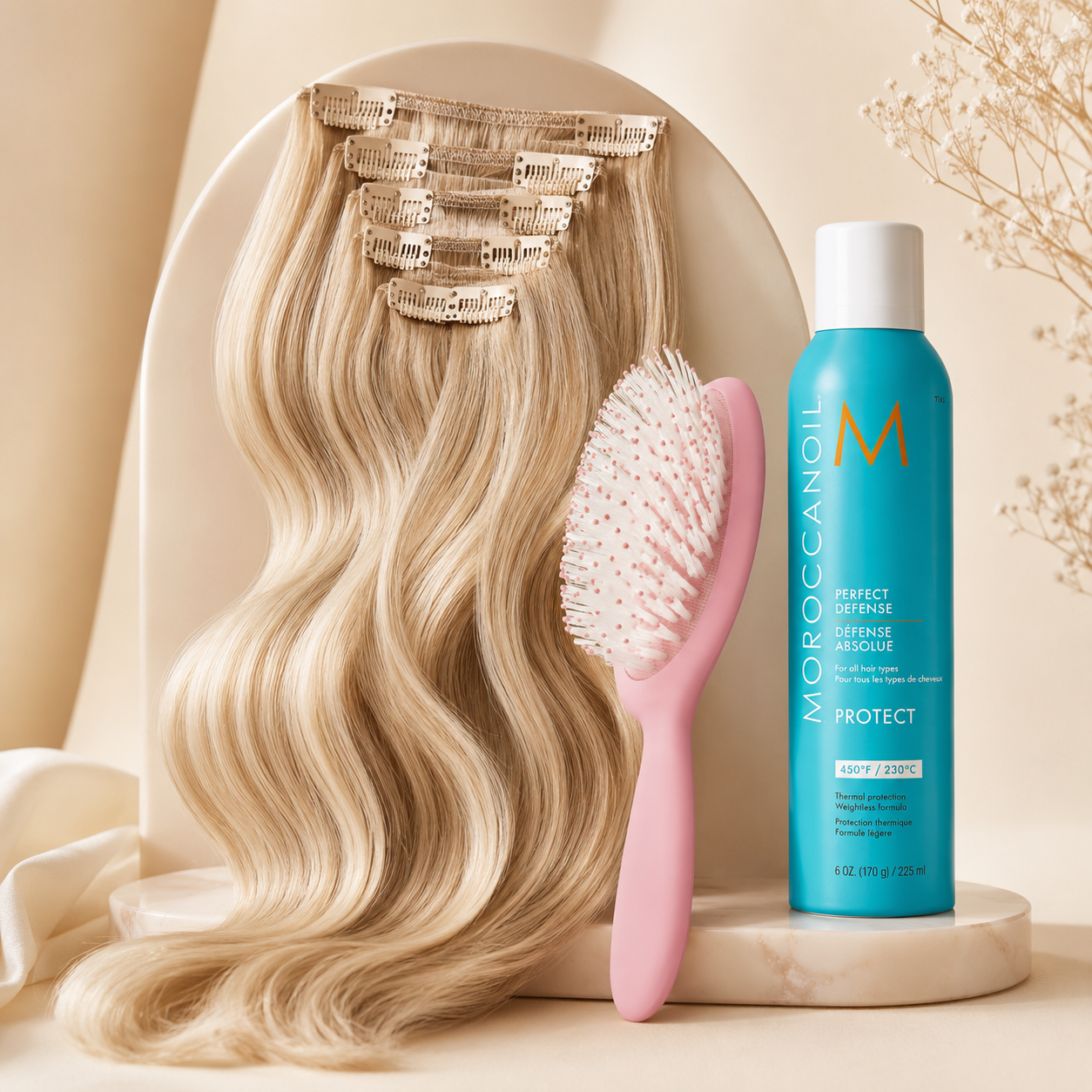 Moroccanoil Protect hair extension set featuring a large wavy blonde extension piece with gold clips, a pink hairbrush, and a turquoise aerosol can on a beige studio set.