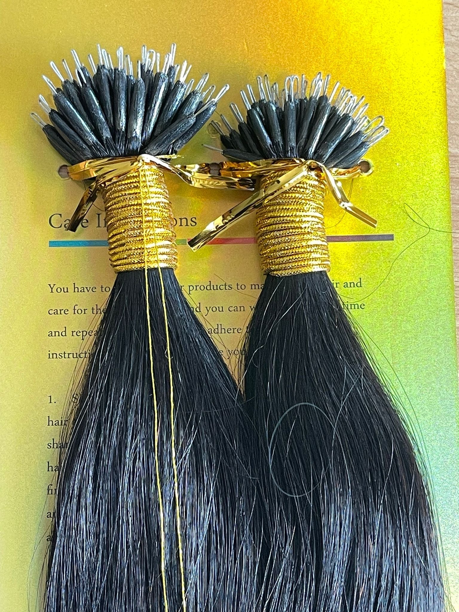 Two bundles of black hair extensions with gold ties on a yellow background.