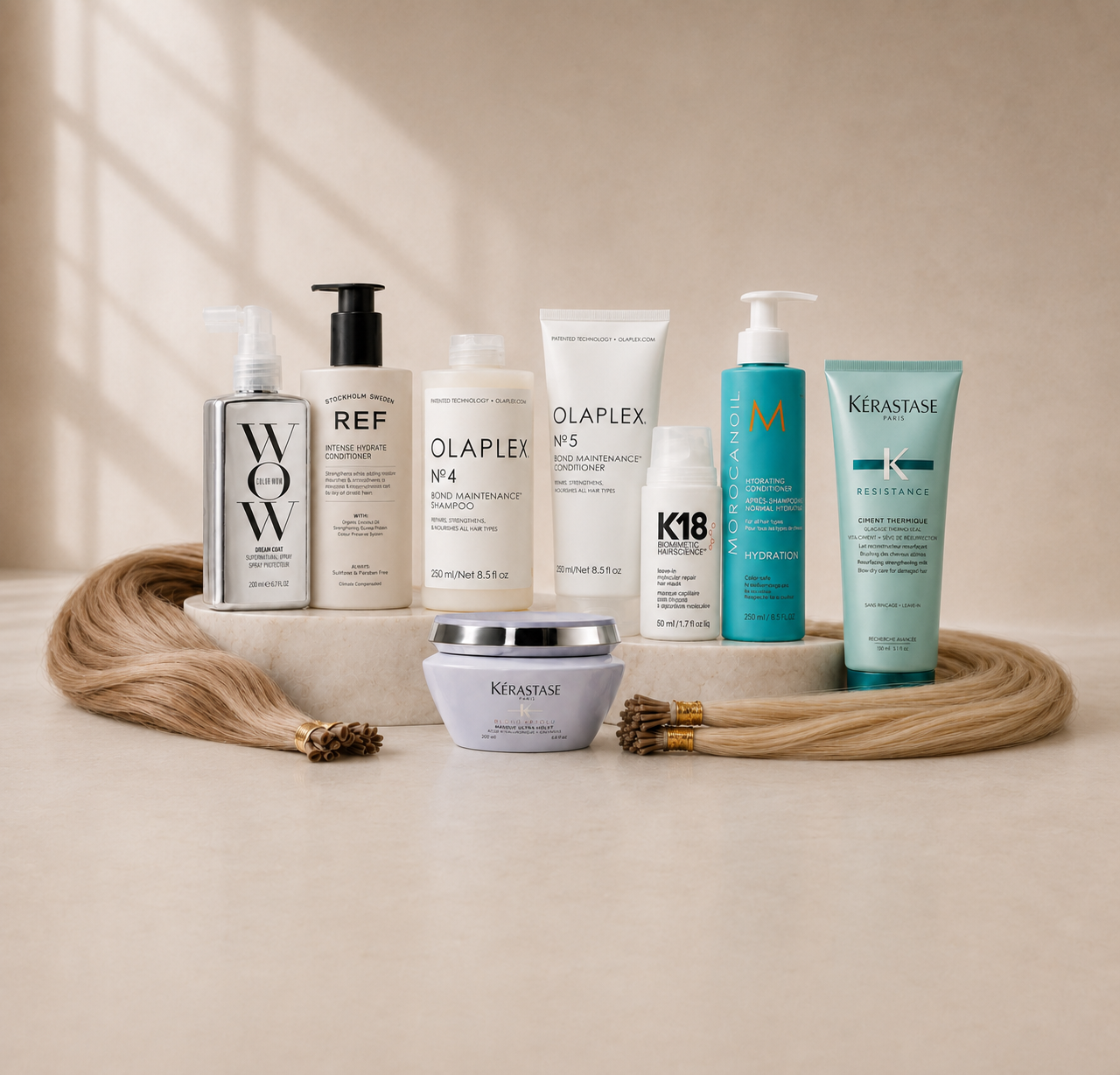 Luxury hair extension aftercare products including Colour Wow, REF, Olaplex, K18, Moroccanoil and Kérastase displayed with blonde hair extensions on a neutral marble background.